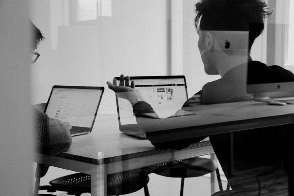 Two people discussing ideas and using laptops.